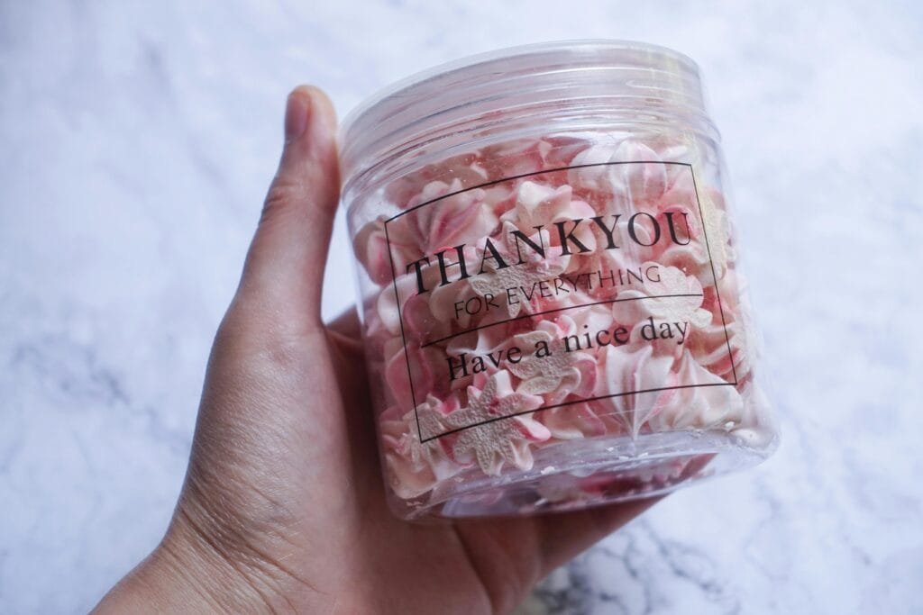 Close-up of a hand holding a jar of pink meringue cookies with a 'Thank you' message.