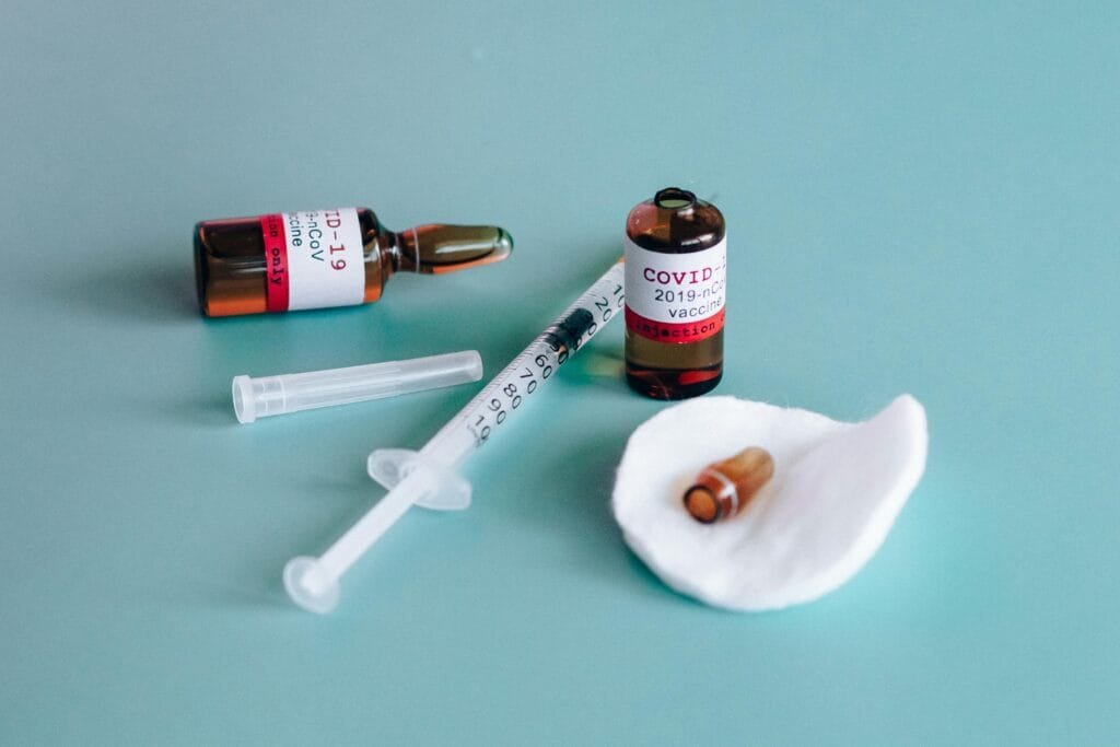 Close-up of COVID-19 vaccine vials with syringe on a teal surface, highlighting medical themes.