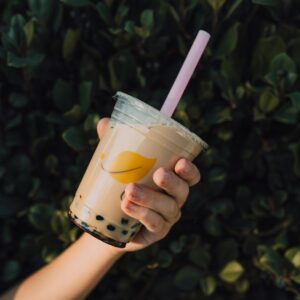 Close-up of a hand holding a refreshing milk tea with boba, outdoors against greenery.