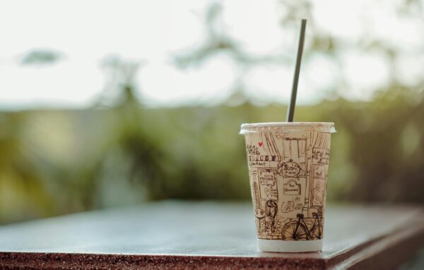 Close-up of a designed paper cup with a straw on a table outdoors, exuding a vintage charm.