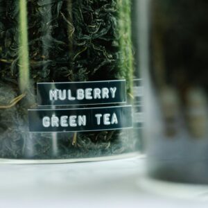 Detailed view of dried mulberry green tea leaves in a labeled glass jar.